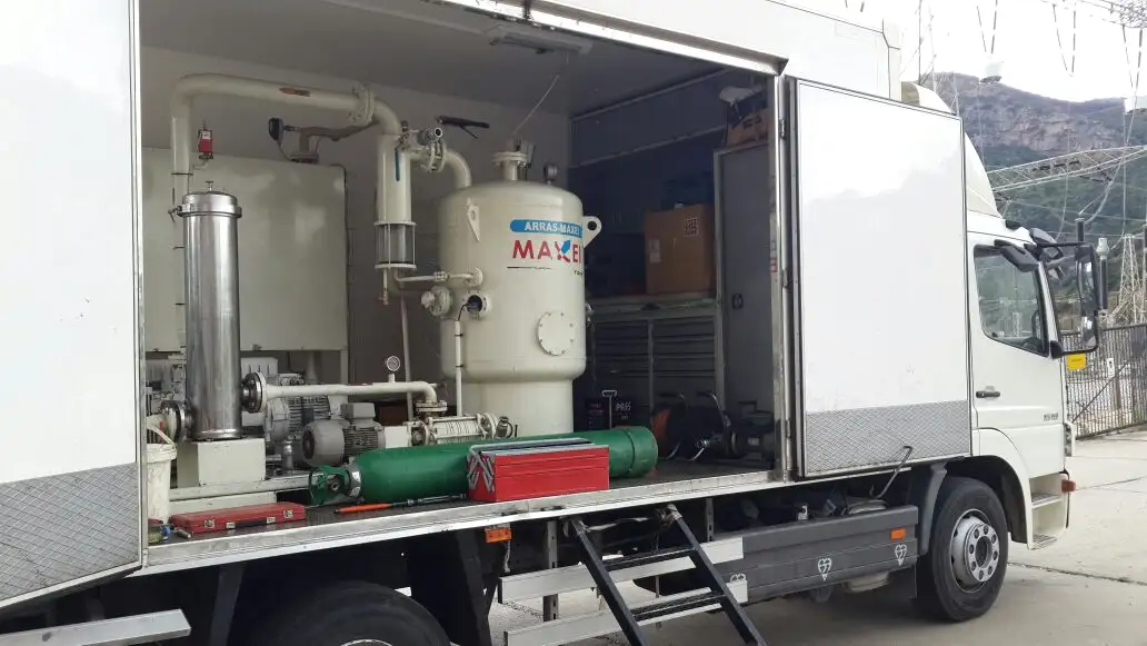 Inside an open truck body: the vacuum vessel, filter housing, pumps and pipework of an oil-treatment plant, with a gas cylinder and tool cases stowed alongside