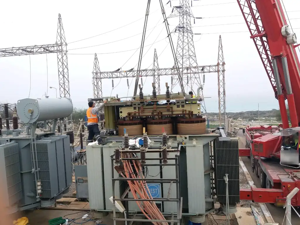 A transformer active part suspended above its tank in an outdoor switchyard, fitters working on top of the tank and a red mobile crane alongside